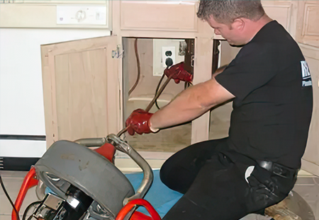 Drain cleaning technician under sink